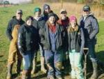 8 men and women wearing winter clothing standing in a grassy field