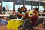 student talks with two students sitting at a table at an organization fair