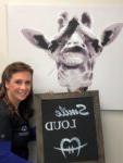 woman holding a sign that reads smile loud with an image of a giraffe wearing braces behind her