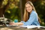 young woman sitting at a table outdoors with a laptop and school supplies