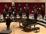 Choir director on stage with 12 choir members on risers singing